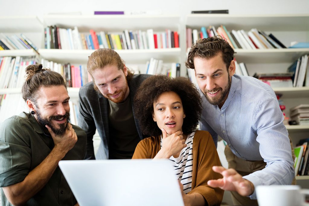 Profissionais em uma sala de reunião moderna conversando sorridentes com um cliente, apresentando dados em um tablet e fortalecendo o relacionamento estratégico.