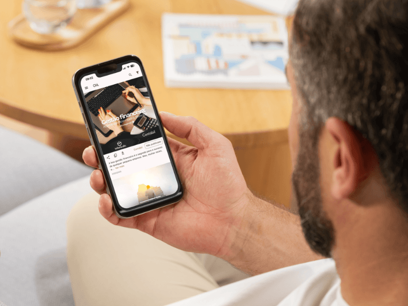 Smartphone que exibe a tela inicial de um aplicativo contábil com gráficos financeiros, área de login do cliente e notificações de guias de impostos.